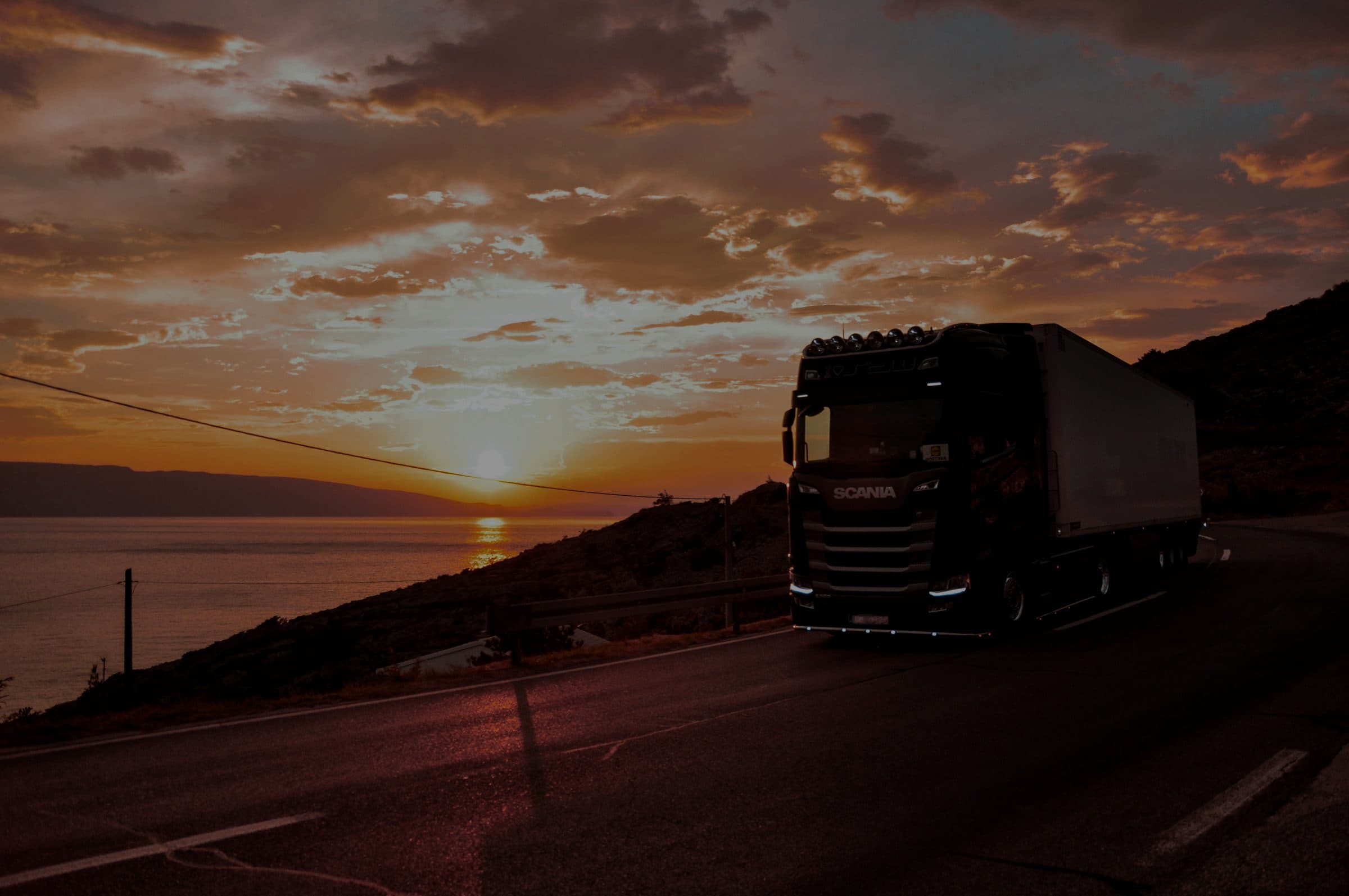Caminhão em rodovia litorânea ao entardecer, representando o transporte da DTM Logística